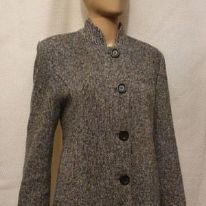 Könnte beinhalten: Graue Tweedjacke mit Stehkragen und drei schwarzen Knöpfen. Die Jacke hat lange Ärmel und ein strukturiertes Aussehen, geeignet für Business oder Freizeit.