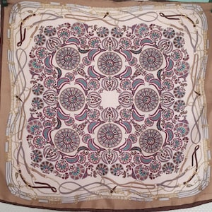 May include: Square silk scarf with a beige background and a detailed floral pattern in teal, burgundy, and cream. The border features a brown trim and a design of belts and chains.