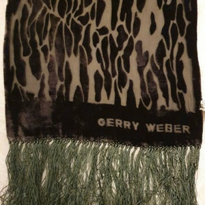 May include: A dark scarf with a pattern of black shapes on a lighter background. The scarf has a dark border with the text "GERRY WEBER" and a fringe of green threads.