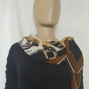 May include: A patterned silk scarf with a mix of geometric and abstract designs in black, brown, beige, and gold. The scarf is draped around a mannequin's neck, with the word "Vieyon" visible on the fabric.