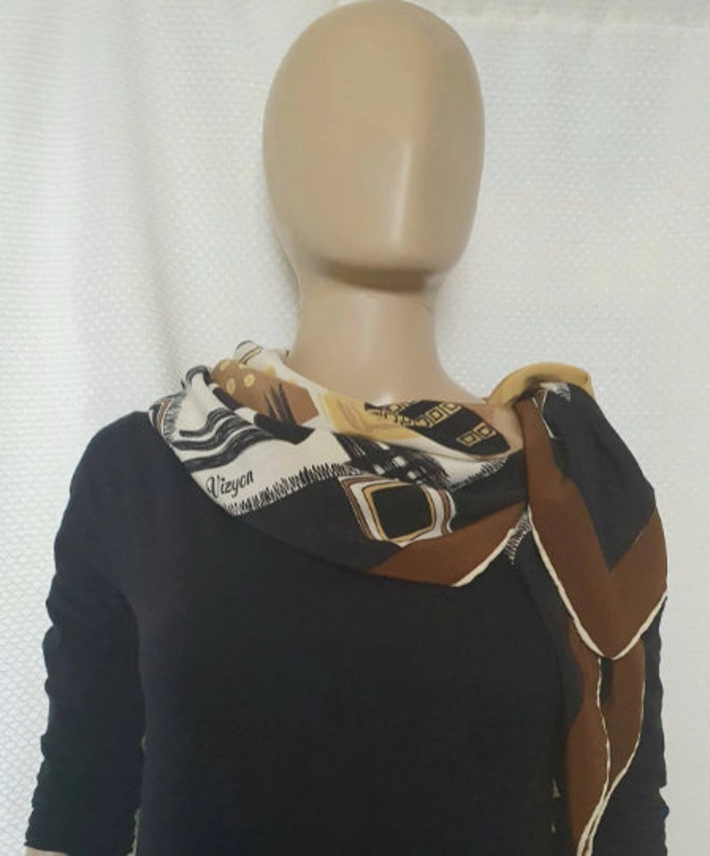 May include: A patterned silk scarf with a mix of geometric and abstract designs in black, brown, beige, and gold. The scarf is draped around a mannequin's neck, with the word "Vieyon" visible on the fabric.