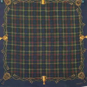May include: A square, navy blue scarf with a plaid pattern in green, red, and yellow. The border features gold-colored trophy and rope designs. The word "PENDLETON" is printed in white on the bottom right corner.