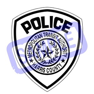 Puede incluir: Una placa de policía en blanco y negro con la palabra «POLICE» en la parte superior. La placa presenta el texto «METROPOLITAN TRANSIT AUTHORITY HARRIS COUNTY» alrededor de un diseño de estrella central. La placa tiene forma de escudo.