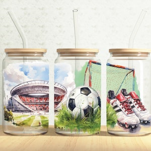 May include: Three glass jars with wooden lids and clear drinking straws. Each jar has a different design: a football stadium, a football with a goal net, and a pair of football boots.