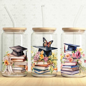 May include: Three clear glass tumblers with bamboo lids and glass straws. Each tumbler features a watercolor design of a graduation cap atop a stack of books, adorned with flowers. One has a butterfly.