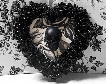 May include: Black heart-shaped wreath with a skull in the center. The wreath is made of black roses and the skull is made of black resin.