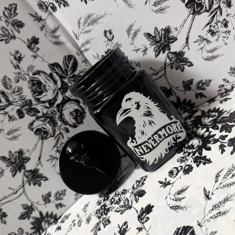 May include: Black glass jar with a white raven design and the text "Nevermore" on a white ribbon. The jar has a black lid.