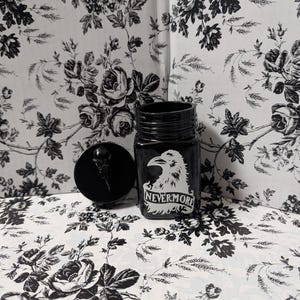 May include: Black glass jar with a black crow and the text "Nevermore" in white. The jar has a black screw-on lid.