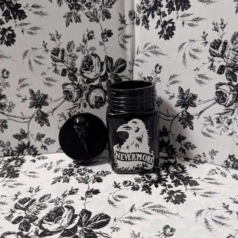 May include: Black glass jar with a black crow and the text "Nevermore" in white. The jar has a black screw-on lid.