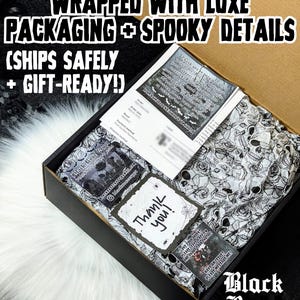 Op de afbeelding: Een zwarte doos met zwart-wit schedel- en rozenpatroon vloeipapier. De doos bevat een bon, een bedankkaart met een spinnenwebontwerp en andere kaarten. Tekst op de doos luidt "EVERY ORDER IS CAREFULLY WRAPPED WITH LUXE PACKAGING + SPOOKY DETAILS".