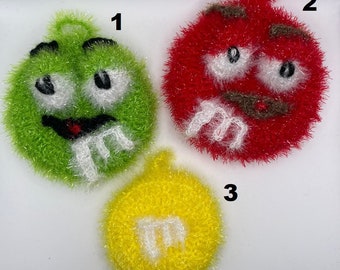 Puede incluir: Tres estropajos de cocina de ganchillo con forma de caramelos M&M. Los estropajos son verdes, rojos y amarillos con M blancas. Los estropajos están numerados del 1 al 3.