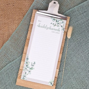 Könnte beinhalten: Ein Holz-Klemmbrett mit einer silbernen Klammer, die einen linierten Notizblock hält. Der Notizblock hat einen hellgrauen Rand und ist mit Aquarell-Eukalyptusblättern verziert. Der Text "der kühlschrank ist leer" ist aufgedruckt.