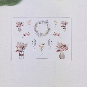 Puede incluir: Una hoja de pegatinas rectangular con ilustraciones en acuarela de arreglos florales secos en jarrones, una corona circular y ramitas botánicas individuales en tonos tierra apagados. El texto Nadines Papeterie está impreso en la parte inferior.