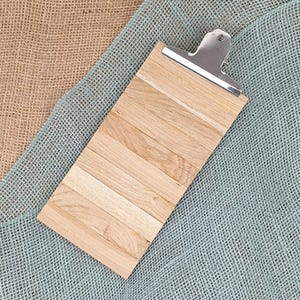 Puede incluir: Un portapapeles rectangular construido con varias l&aacute;minas de madera de color marr&oacute;n claro dispuestas horizontalmente una al lado de la otra. La parte superior cuenta con un mecanismo de clip de metal plateado pulido.