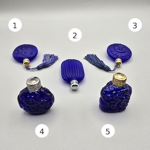 Pode incluir: Uma variedade de cinco frascos de perfume e tampas de vidro azul cobalto. Os frascos apresentam várias formas e texturas, incluindo designs redondos, ovais e canelados. Alguns têm detalhes decorativos em metal dourado ou prateado e borlas a condizer.