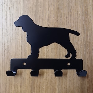 May include: Black metal key hook shaped like a cocker spaniel silhouette. The hook has three hooks on the bottom.