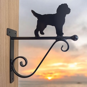 May include: Black metal silhouette of a dog mounted on a black metal bracket with a scroll design. The bracket is attached to a wooden wall.
