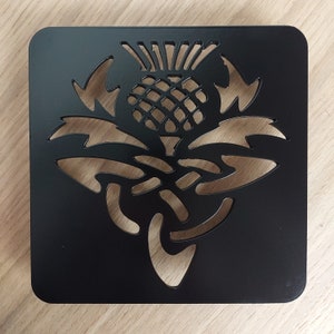 May include: Black metal coaster featuring a cut-out design of a stylised thistle flower.