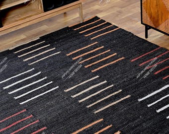 May include: A rectangular area rug featuring a dark black base with repeating geometric patterns of horizontal lines in white, beige, and terracotta orange. The rug has a textured, woven appearance and is positioned on a wooden floor.