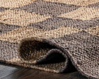 Puede incluir: Primer plano de una alfombra de yute marrón y beige con un patrón de chevron. La alfombra está doblada, mostrando la textura de las fibras tejidas.