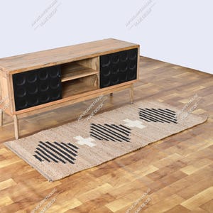 May include: A rectangular jute runner rug featuring a natural tan base with a repeating geometric pattern of black stripes and white cross shapes. The rug is positioned on a wooden floor in front of a wooden media console with two black doors.