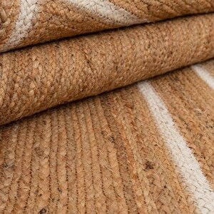 Puede incluir: Una alfombra de fibra natural con un patr&oacute;n tejido de rayas blancas sobre un fondo marr&oacute;n. La alfombra est&aacute; hecha de yute y es perfecta para agregar un toque de textura natural a cualquier habitaci&oacute;n.