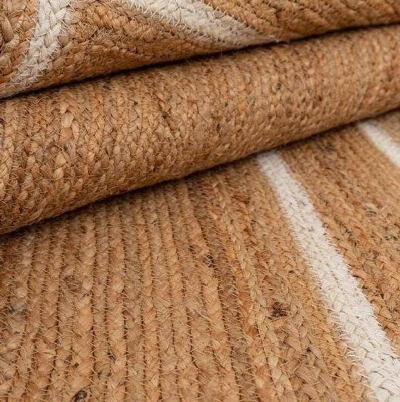 Puede incluir: Una alfombra de fibra natural con un patr&oacute;n tejido de rayas blancas sobre un fondo marr&oacute;n. La alfombra est&aacute; hecha de yute y es perfecta para agregar un toque de textura natural a cualquier habitaci&oacute;n.