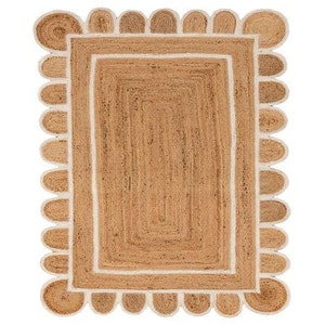 Puede incluir: Una alfombra de fibra natural con un borde blanco y un borde festoneado. La alfombra est&aacute; hecha de yute y tiene un color natural y terroso.
