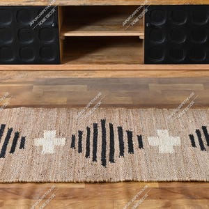 May include: A rectangular woven jute runner rug featuring a repeating pattern of black vertical stripes and white cross shapes. The rug is positioned on a wooden floor in front of a wooden media console with two black cabinet doors.