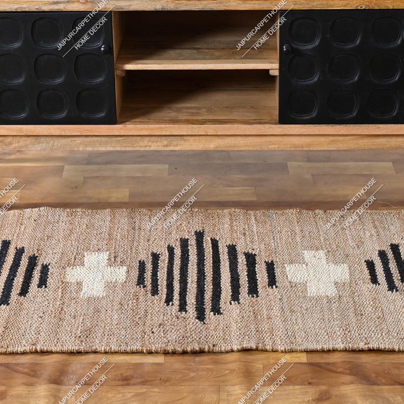 May include: A rectangular woven jute runner rug featuring a repeating pattern of black vertical stripes and white cross shapes. The rug is positioned on a wooden floor in front of a wooden media console with two black cabinet doors.