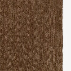 Puede incluir: Primer plano de una alfombra tejida marr&oacute;n con una superficie texturizada. La alfombra tiene un patr&oacute;n de tejido apretado y un tono c&aacute;lido y terroso. Las fibras de la alfombra son visibles, creando una apariencia t&aacute;ctil. La alfombra es adecuada para la decoraci&oacute;n del hogar.