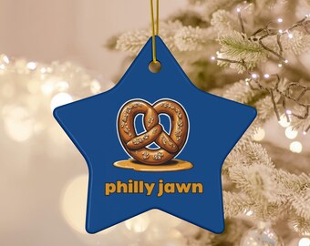Op de afbeelding: Een blauwe stervormige kerstversiering met een bruine pretzel en de tekst "philly jawn" in geel.