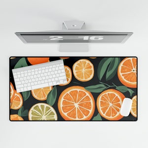 May include: A black and white keyboard sits on a desk mat with a pattern of orange slices and green leaves. The mat is a desk accessory for a computer.