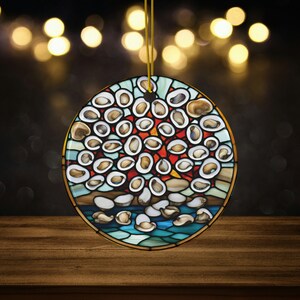 May include: A round ceramic ornament with a stained glass design of a cluster of oyster shells in shades of blue, red, and white. The ornament is hanging from a gold string.