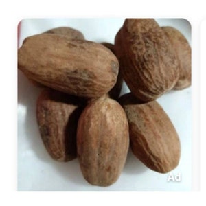 May include: A close-up of a group of brown whole nutmeg spices. The nutmeg is arranged on a white surface.