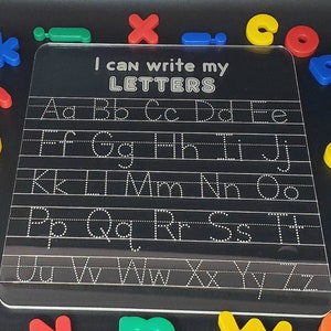 May include: A clear plastic dry-erase board with dotted lines for tracing letters. The board has the text "I can write my LETTERS" at the top.  The letters of the alphabet are written in rows on the board.
