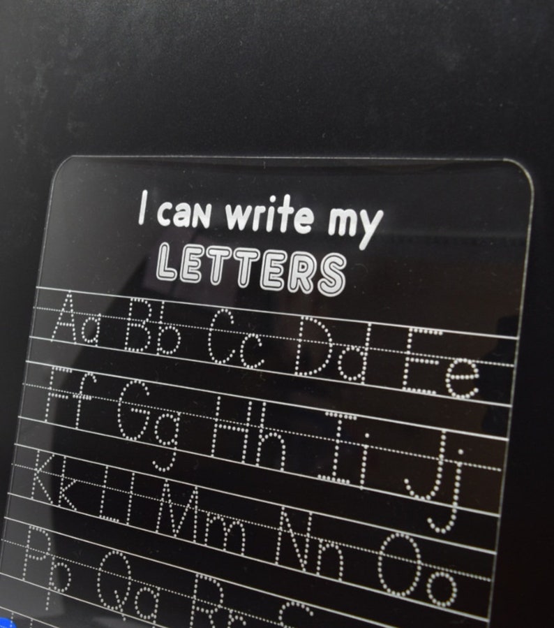 May include: A black dry-erase board with white dotted lines and letters for practicing writing the alphabet. The board has the text "I can write my LETTERS" at the top.