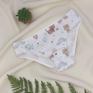 Puede incluir: Ropa interior blanca con un estampado repetido de animales de dibujos animados, arcoíris, globos y estrellas. La ropa interior tiene un borde festoneado y un corte de cintura baja. Los colores incluyen rosa, azul, marrón y tonos pastel.
