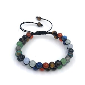 Puede incluir: Un brazalete de cuentas multicolores con un cordón negro y un cierre ajustable. Las cuentas están hechas de varias piedras preciosas, incluyendo ojo de tigre, lapislázuli y amatista.