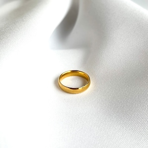 Könnte beinhalten: Ein einfacher goldener Ring auf einem weißen Stoffhintergrund.