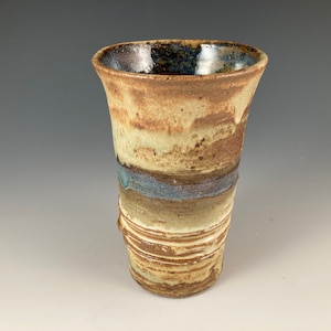 May include: A brown and white ceramic vase with a blue glaze. The vase has a flared top and a rounded bottom.