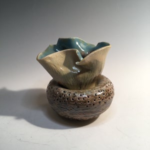 May include: A ceramic vase with a textured brown base and a light blue and yellow ruffled top.