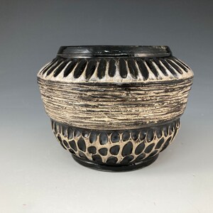 May include: A black and white ceramic planter with a textured design. The planter has a wide, round base and a narrow opening.