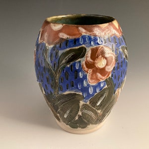 May include: A ceramic vase with a floral design. The vase is decorated with brown, blue, and green flowers and leaves. The vase has a rounded shape and a white background.