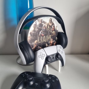 May include: A white wireless gaming headset with a Call of Duty themed design on the earcups. The headset is sitting on a white stand with a white wireless controller.