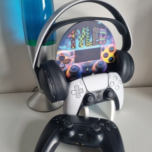 May include: A white and black PlayStation 5 controller with a colorful, custom-designed headset stand. The stand features a colorful design with the text "TYLER" in the center.