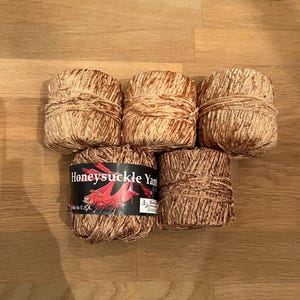 May include: Five skeins of Honeysuckle Yarn in shades of brown and tan. The yarn is arranged on a wooden surface. One skein has a label that reads "Honeysuckle Yarn" with a floral design.