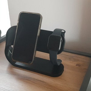 Könnte beinhalten: Ein schwarzer Ladeständer mit einem Telefon und einer Uhr darauf. Der Ständer steht auf einer Holzoberfläche.