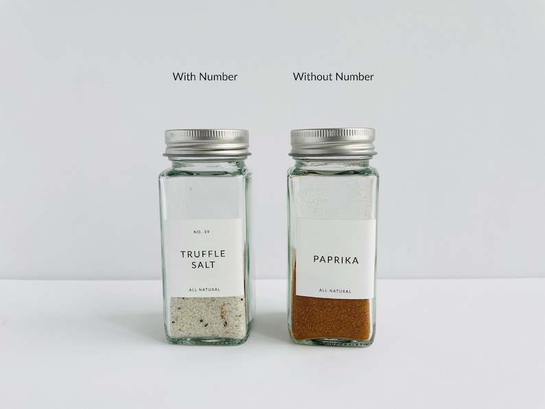 以下が含まれることがあります： 銀色の蓋が付いた2つの透明なガラス製スパイスジャー。1つは「Truffle Salt」、もう1つは「Paprika」とラベル付けされています。どちらのジャーにも、黒い文字の白いラベルが付いています。「Truffle Salt」ジャーには「No. 39」のラベルが付いています。