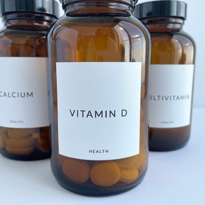 May include: Three amber glass bottles with white labels and black lids. The labels read "Calcium", "Vitamin D", and "Multivitamin". Each bottle contains round, orange pills.